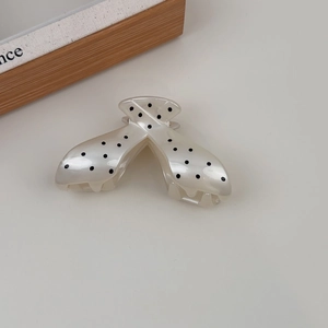 Close-up of large hair claw clip featuring black polka dots on cream acetate surface