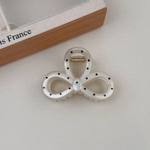 Close-up of elegant French polka dot bow hair claw clip with gold spring and pearly finish
