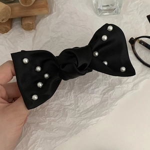 Détail d'une élégante pince à cheveux en satin noir ornée de perles blanches et soyeuses