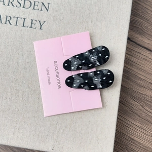 Close-up of French style black and white polka dot hair clips on a pink display card