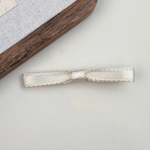 Macro detail of creamy satin ribbon bow hair clip with delicate woven texture edge