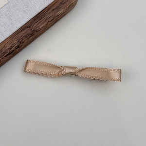 Detail of champagne bow hair clip with textured ribbon and delicate scalloped edges