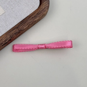 Detailed view of pink ribbon bow hair clip with delicate wavy edges and satin texture