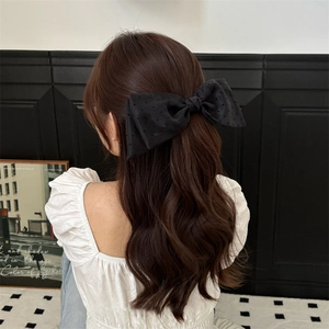 Polka dot black bow hair clip shown on model with dark brown wavy hair in chic setting