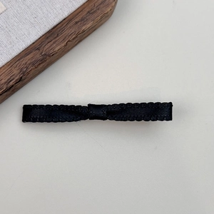 Detail of a handmade black ribbon bow hair clip with textured satin finish on gray surface