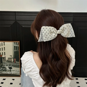 Rear view of a large white polka dot mesh bow hair clip on long wavy brown hair