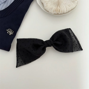 Close-up of black polka dot sheer mesh bow hair clip on a soft cream background