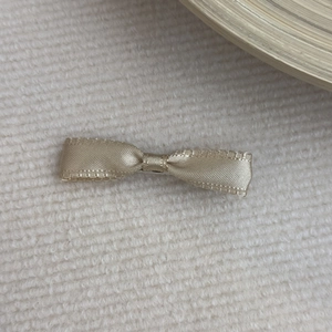 Close-up of champagne gold satin bow hair clip with wavy edges on white knit fabric