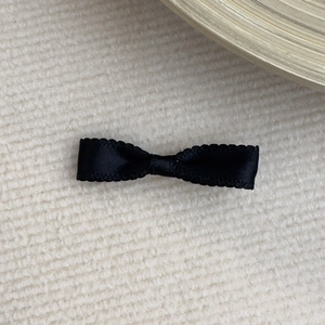 Close-up of black satin ribbon bow hair clip with wavy edges on white knit background
