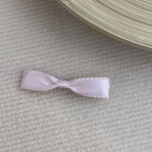 Detail of pink satin ribbon bow with lace edges on a cream knitted background