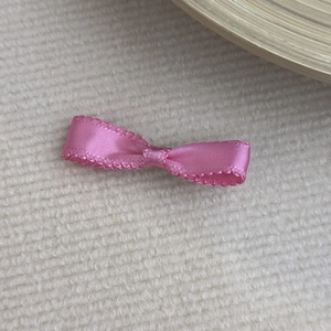 Detail of pink satin bow hair clip with scalloped edges on white knitted fabric