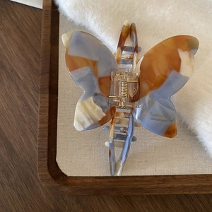 Close-up of butterfly hair claw clip with blue and orange marble texture and gold spring