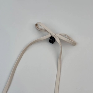 Détail de la pince à cheveux avec nœud en similicuir crème et rubans élégants
