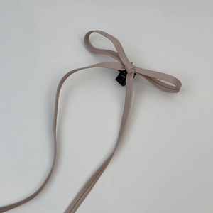 Détail de la barrette à nœud en cuir rose poudré avec de longs rubans pendants