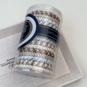 Close-up of durable braided hair ties in a minimalist cylindrical jar with various neutral colors