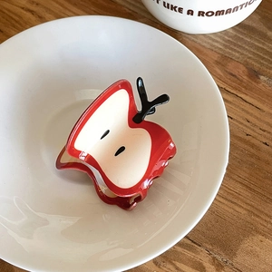 Detailed macro view of a red apple slice hair claw clip inside a white ceramic bowl