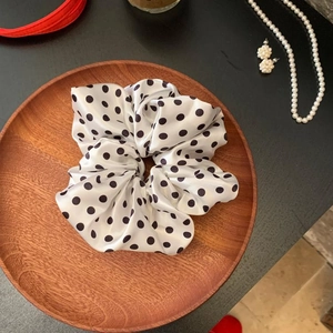 Close-up of a white satin scrunchie with black polka dots on a wooden tray with jewelry
