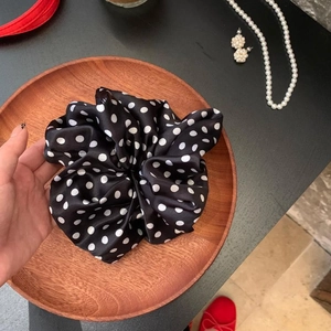 Detailed close-up of a black and white polka dot silk scrunchie on a wooden tray