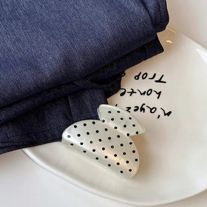 Nahaufnahme einer cremefarbenen Haarklammer mit Punkten auf Denim und einem Keramiktablett