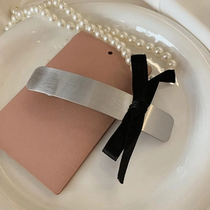 Détail du pince à cheveux en argent brossé avec un nœud en satin noir sur carte rose