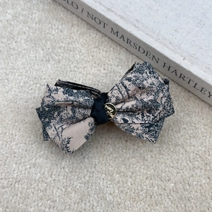 Close-up of Toile de Jouy print bow hair claw with elegant golden metal relief button