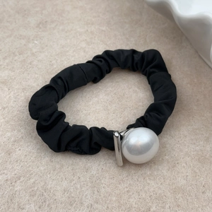 Detail of minimalist black scrunchie with textured fabric and large white pearl accent