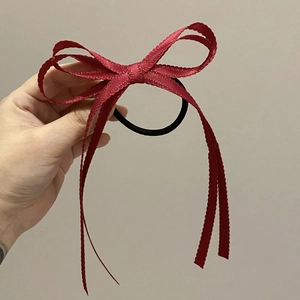 Dettaglio di un elastico per capelli con fiocco in nastro rosso scuro e bordi seghettati
