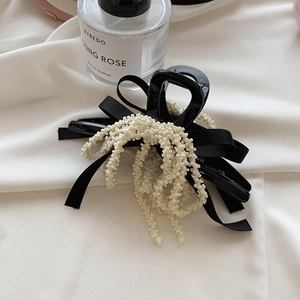 Detail view of a black bow hair claw clip with elegant pearl tassels on silk fabric