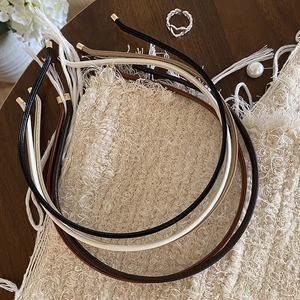 Minimalist PU leather headbands set with gold metal end caps on a rustic textured surface