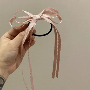Dettaglio di un elastico per capelli rosa con fiocco e bordi ondulati chic
