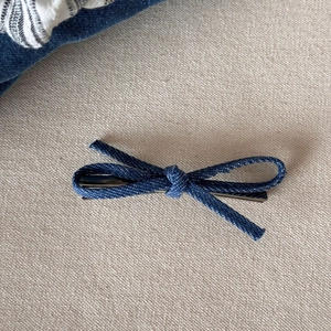 Detail van blauwe denim strik haarclip met zilveren metalen clip op beige getextureerde stof