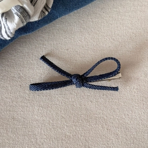 Detail van donkerblauwe denim strik haarclip met zilveren metalen klem op beige ondergrond