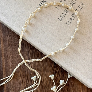 Detail of bohemian braided headband with white pearls and floral charm on wooden desk