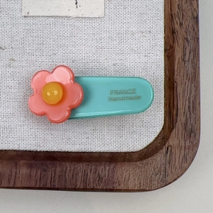 Macro shot of a blue acetate hair clip with a pink flower and handmade lettering