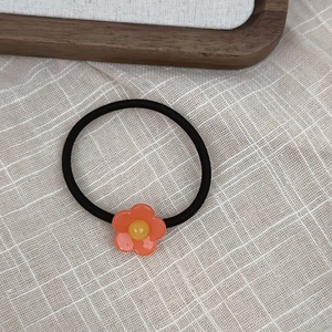 Close-up of a floral acetate hair tie with orange petals on a beige linen background