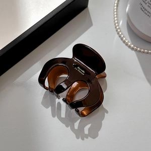 Detailed close-up of dark brown glossy acetate hair claw clip with golden lettering
