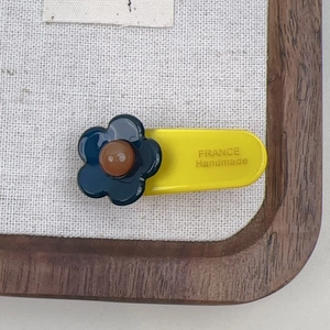 Detail of yellow acetate hair clip featuring a blue flower and France Handmade text