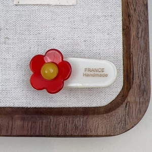 Detail view of a handmade acetate flower hair clip with a red floral design and gold text