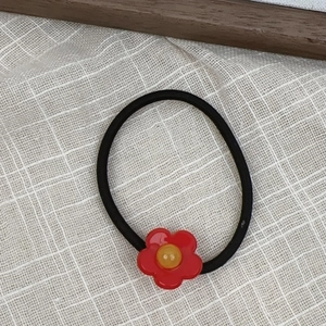 Macro view of a red acetate flower hair tie with a yellow center on white grid fabric