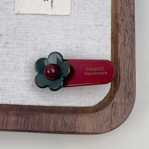 Close-up of a handmade floral hair clip featuring a green flower and gold France branding
