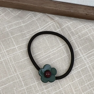 Detailed close-up of a green flower hair tie with red bead on a beige fabric background