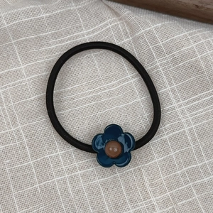 Detail of high-elastic black hair tie with deep blue resin flower and brown center bead