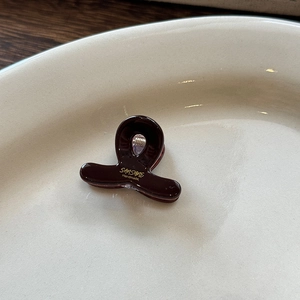 Dettaglio di una molletta per capelli in acetato di lusso con scritte dorate su vassoio