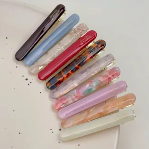 Set of 10 colorful acetate hair clips with gold metal base on a beige ceramic plate