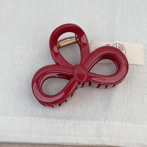 Détail macro d'une pince à cheveux nœud bordeaux avec ressort doré sur tissu texturé