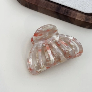 Close-up of an orange and white marble acetate hair claw clip with a glossy finish