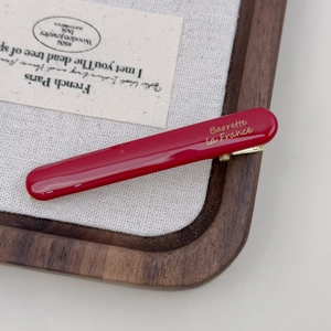 Elegant red acetate hair clip with gold lettering on a vintage textured linen background