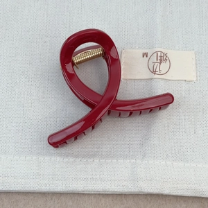 Détail d'une pince à cheveux bordeaux brillant avec ressort doré sur lin blanc