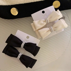 Elegant satin bow hair clips with pearls in black and cream on decorative packaging