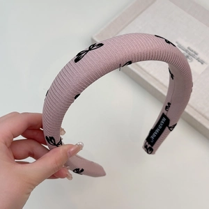 Détail d'un serre-tête rose rembourré avec motifs de nœuds noirs et étiquette faite main